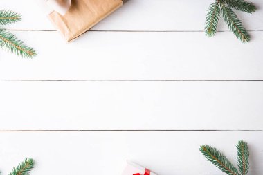 Noel hediyesi kutuları, karlı köknar dalları, kozalaklı kozalaklar, tarçınlı kurutulmuş meyveler, bayram süslemeleri, karamel çubukları olan ahşap beyaz arka planda güzel bir Noel kompozisyonu. Yeni yıl. Üst görünüm, alanı kopyala.