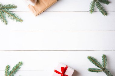 Noel hediyesi kutuları, karlı köknar dalları, kozalaklı kozalaklar, tarçınlı kurutulmuş meyveler, bayram süslemeleri, karamel çubukları olan ahşap beyaz arka planda güzel bir Noel kompozisyonu. Yeni yıl. Üst görünüm, alanı kopyala.