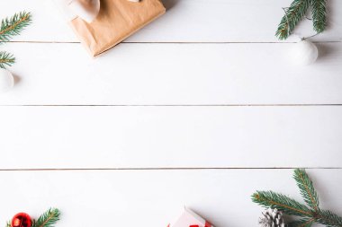 Noel hediyesi kutuları, karlı köknar dalları, kozalaklı kozalaklar, tarçınlı kurutulmuş meyveler, bayram süslemeleri, karamel çubukları olan ahşap beyaz arka planda güzel bir Noel kompozisyonu. Yeni yıl. Üst görünüm, alanı kopyala.