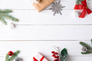 Noel hediyesi kutuları, karlı köknar dalları, kozalaklı kozalaklar, tarçınlı kurutulmuş meyveler, bayram süslemeleri, karamel çubukları olan ahşap beyaz arka planda güzel bir Noel kompozisyonu. Yeni yıl. Üst görünüm, alanı kopyala.