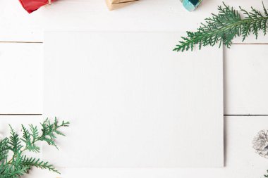 Noel hediyesi kutuları, karlı köknar dalları, kozalaklı kozalaklar, Noel süslemeleri, karamel çubukları olan ahşap beyaz arka planda güzel bir Noel kompozisyonu. Yeni yıl. Üst görünüm, alanı kopyala.