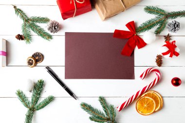 Ahşap beyaz arka planda güzel bir Noel kompozisyonu. Noel hediye kutularının olduğu boş kart, karlı köknar dalları, kozalaklı kozalaklar, karamel çubuğu, hediye. Yeni yıl. Üst görünüm, alanı kopyala.