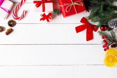 Ahşap beyaz arka planda güzel bir Noel kompozisyonu. Noel hediye kutuları, karlı köknar dalları, kozalaklı kozalaklar, karamel çubuğu, hediye. Yeni yıl. Üst görünüm, alanı kopyala.