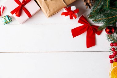 Ahşap beyaz arka planda güzel bir Noel kompozisyonu. Noel hediye kutuları, karlı köknar dalları, kozalaklı kozalaklar, karamel çubuğu, hediye. Yeni yıl. Üst görünüm, alanı kopyala.