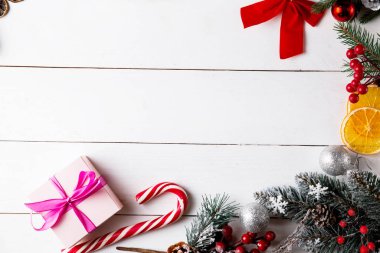 Ahşap beyaz arka planda güzel bir Noel kompozisyonu. Noel hediye kutuları, karlı köknar dalları, kozalaklı kozalaklar, karamel çubuğu, hediye. Yeni yıl. Üst görünüm, alanı kopyala.