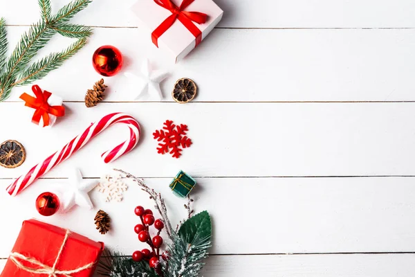 Noel hediyesi kutuları, karlı köknar dalları, kozalaklı kozalaklar, tarçınlı kurutulmuş meyveler, bayram süslemeleri, karamel çubukları olan ahşap beyaz arka planda güzel bir Noel kompozisyonu. Yeni yıl. Üst görünüm, alanı kopyala.