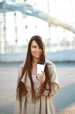 Sokakta yürüyen bir fincan kahveyle güzel bir kadın. Süslü Ofis Giysileri içinde Çekici Genç Bir Kadının Portresi Dışarıda duran Sıcak İçeceklerle Dolu