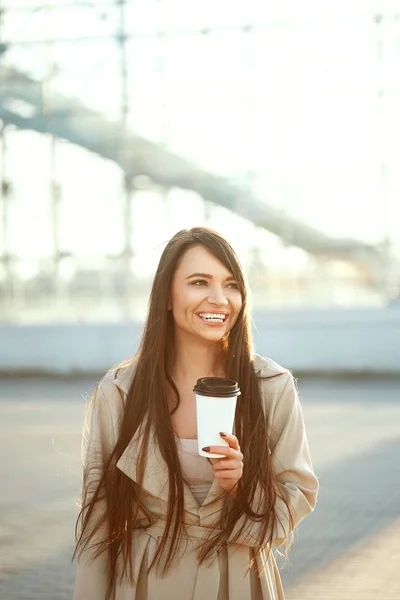Beautiful Woman With Cup Of Coffee Walking On Street. Portrait Of Attractive Young Female In Stylish Office Clothes Holding Cup Of Hot Drink Standing Outdoors