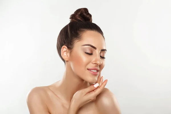 Beautiful smiling woman with healthy smooth facial clean skin applying cosmetic cream and touch own face. Model with  Beauty face. Skin care Moisturizer Facial treatment. Cosmetology. Spa.