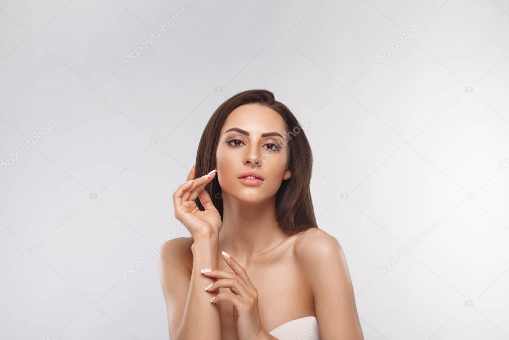 Beautiful young woman with clean perfect skin. Portrait of beauty model with natural nude make up and touching her face. Spa, skin care and wellness. Copyspace.