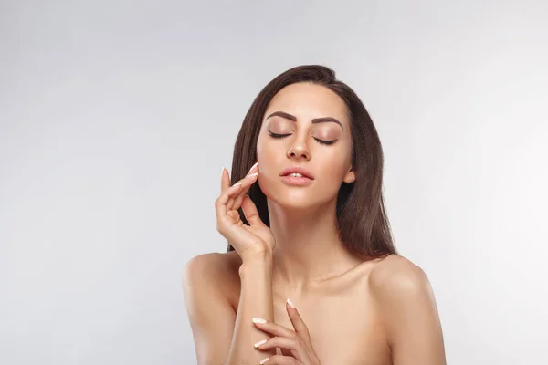 Temiz ciltli güzel bir genç kadın. Doğal çıplak makyajlı ve yüzüne dokunan güzellik modeli portresi. Spa, cilt bakımı ve sağlık. Kopyalama alanı.