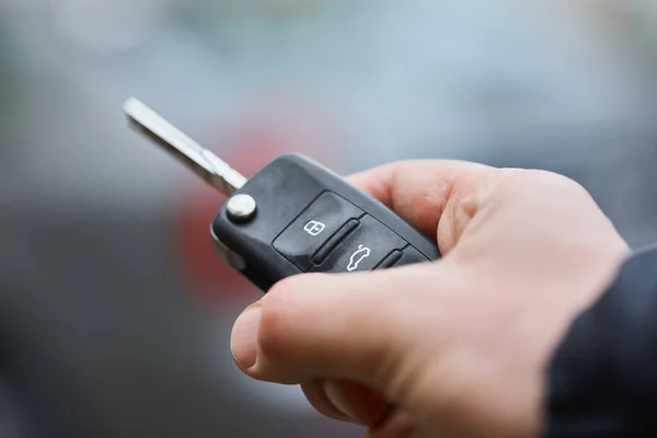 Business man hand holding car keys front with car on background. parking in front of the house. transportation concept