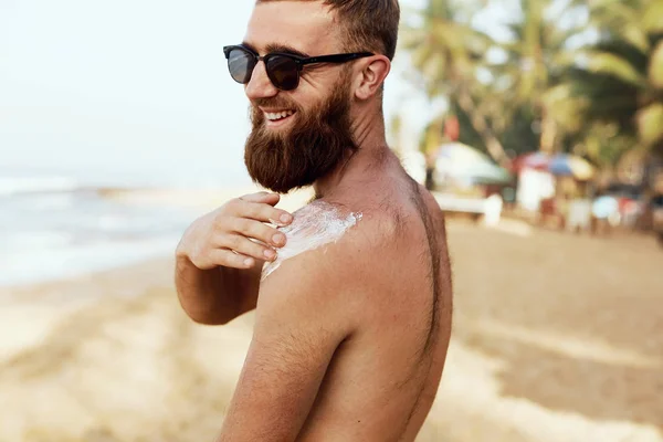 Handsome Man with beard, In Sunglasses Sunbathing With Sunscreen Lotion Body In Summer. Male Fitness Model Tanning Using Solar Block Cream For Healthy Tan. Skincare. Sun Skin Protection