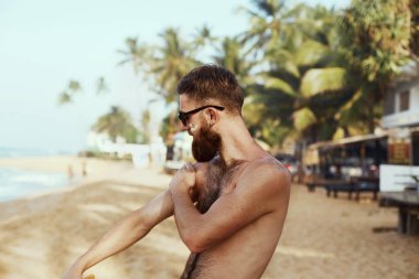 Güneş kremi sürmüş güneş gözlüklü, sakallı yakışıklı adam. Sağlıklı Bronzlaşma İçin Erkek Spor Modeli Güneş Kremi Kullanıyor. Cilt bakımı. Güneş Cildi Koruması 