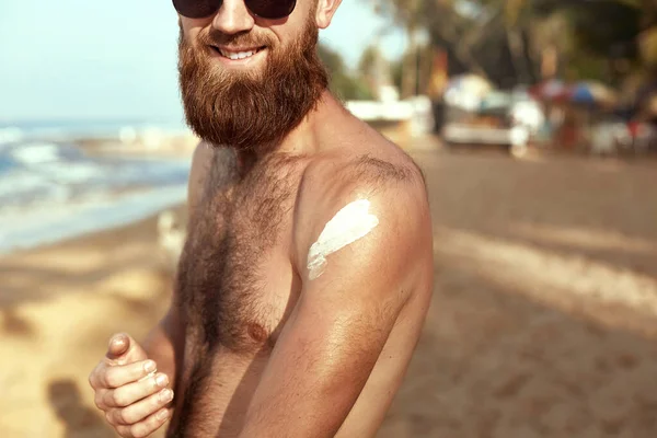 Handsome Man with beard, In Sunglasses Sunbathing With Sunscreen Lotion Body In Summer. Male Fitness Model Tanning Using Solar Block Cream For Healthy Tan. Skincare. Sun Skin Protection