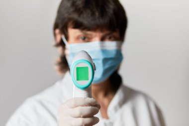 Koruyucu maske takan doktor vücut ısısını kontrol etmek için kızılötesi alın termometresi kullanmaya hazır. Salgın virüs salgını konsepti. Coronavirüs. Termometre tabancası.