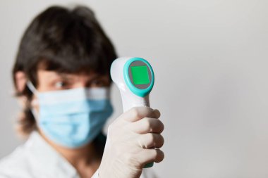 Koruyucu maske takan doktor vücut ısısını kontrol etmek için kızılötesi alın termometresi kullanmaya hazır. Salgın virüs salgını konsepti. Coronavirüs. Termometre tabancası.
