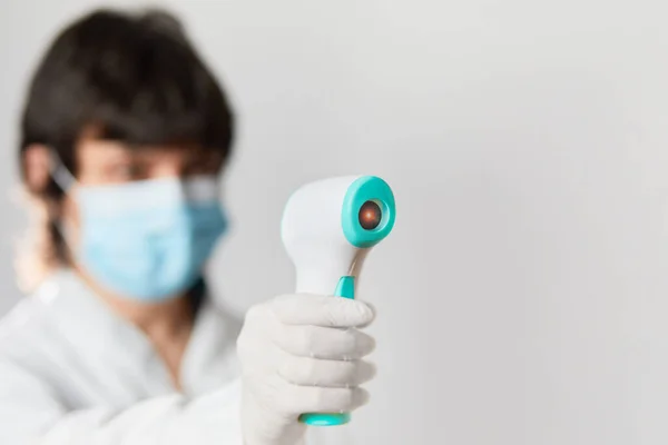 Koruyucu maske takan doktor vücut ısısını kontrol etmek için kızılötesi alın termometresi kullanmaya hazır. Salgın virüs salgını konsepti. Coronavirüs. Termometre tabancası.