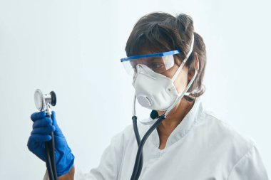 Koruyucu maskeli doktor, hastasını steteskopla incelemeye hazırlanıyor..