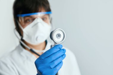 Koruyucu maskeli doktor, hastasını steteskopla incelemeye hazırlanıyor..