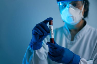 Coronavirus 2019 nCoV kan örneği. Koruyucu eldivenli, maskeli ve gözlüklü bir doktor 2019 nCoV analizi için üzerinde kan olan test tüpü tutuyor. Coronavirus kan testi konsepti. Aşı araştırması