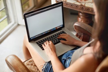 Dizüstü bilgisayarda çalışan bir kadın. İnternette arama yapmak için dizüstü bilgisayar kullanan bir kadın, bilgi taraması, evde iş yeri olması. Bilgisayarlı çalışma alanı. Uzaklık öğrenimi