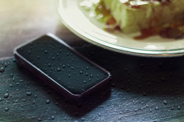 modern smartphone with water drops on food wood table background