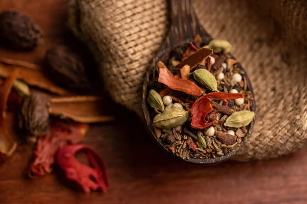 Смешивать специи и травы в деревянной ложке на темном фоне, индийские специи пищи и ингредиенты кухни — стоковое фото