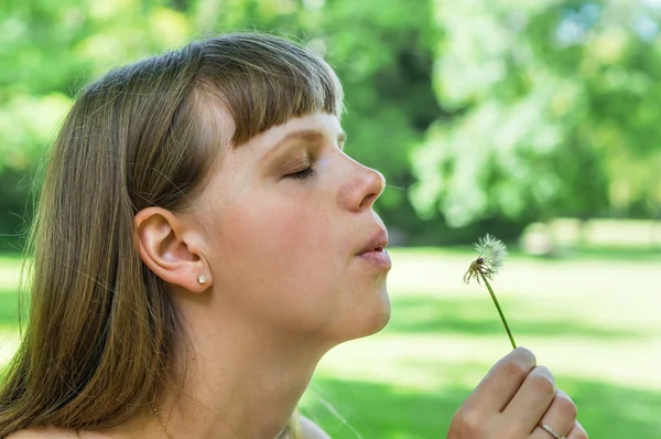 Joven mujer soplando flor de diente de león — Foto de Stock