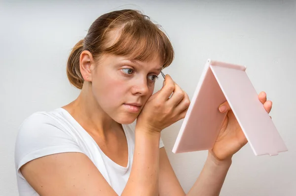 Mujer arrancando cejas con pinzas delante del espejo — Foto de Stock