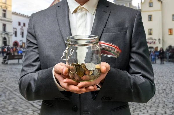 Empresario en traje negro sosteniendo tarro de dinero con monedas —  Fotos de Stock