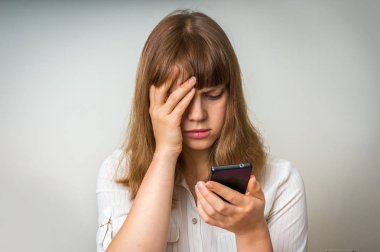 Disappointed woman holding and looking on mobile phone clipart