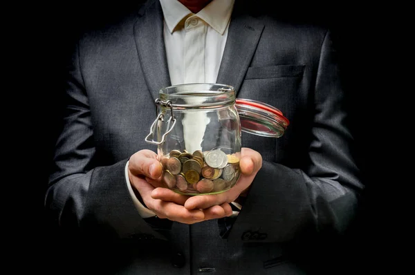 Hombre de traje negro sosteniendo tarro de dinero con monedas —  Fotos de Stock