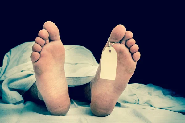 O corpo do morto com etiqueta em branco nos pés sob pano branco — Fotografia de Stock