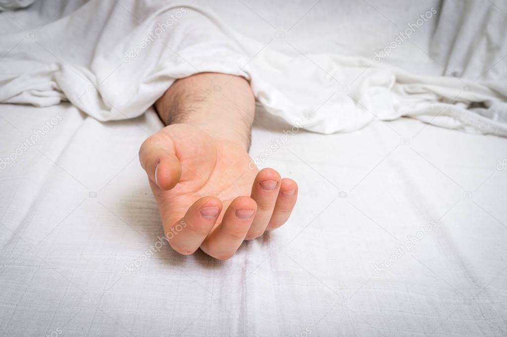 The dead man's body under white cloth with focus on hand