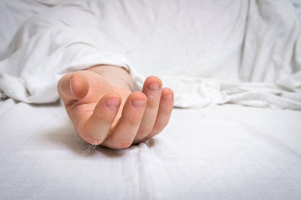 The dead man's body under white cloth with focus on hand