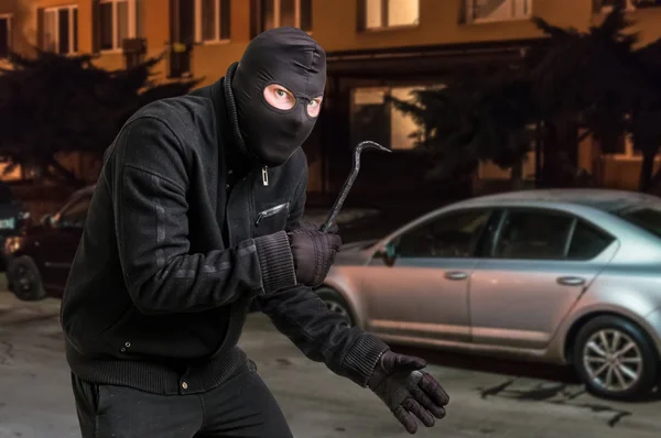 Maskovaný zloděj v kuklu s páčidlem chce vykrást auto — Stock fotografie