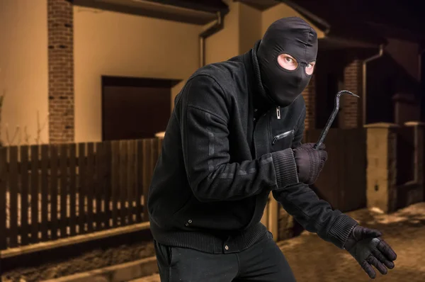 Maskerad tjuv i balaclava med kofot vill råna ett hus — Stockfoto