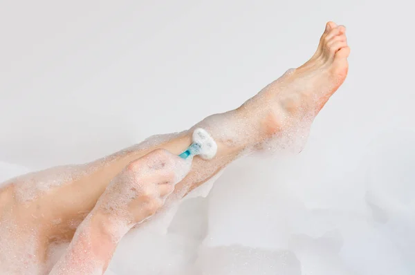 Женщина бреет ноги бритвой в ванной комнате — стоковое фото