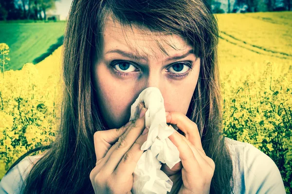 Woman with allergy on yellow rape field sneezing in tissue — Stock Photo, Image