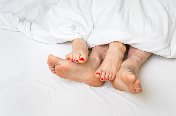 Pés de um casal na cama debaixo do cobertor — Fotografia de Stock