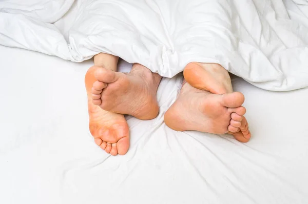 Pies de una pareja en la cama debajo de la manta — Foto de Stock
