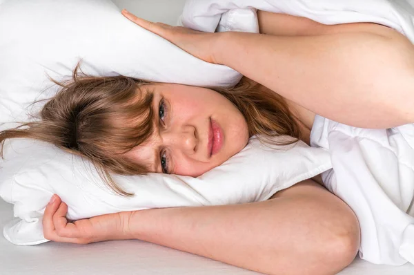 Mulher na cama cobrindo orelhas com travesseiro por causa do ruído — Fotografia de Stock