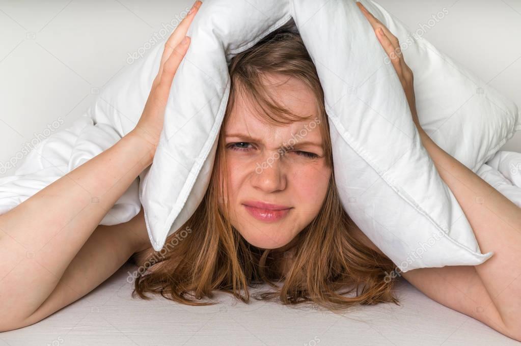 Woman in bed covering ears with pillow because of noise