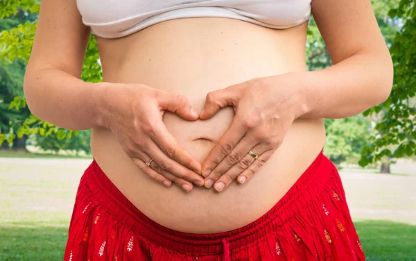 怀孕的妇女，用手在心的形状 — 图库照片