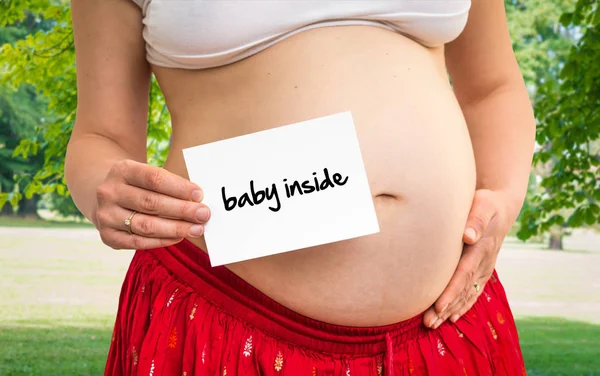 Femme enceinte tenant du papier avec inscription : bébé à l'intérieur — Photo