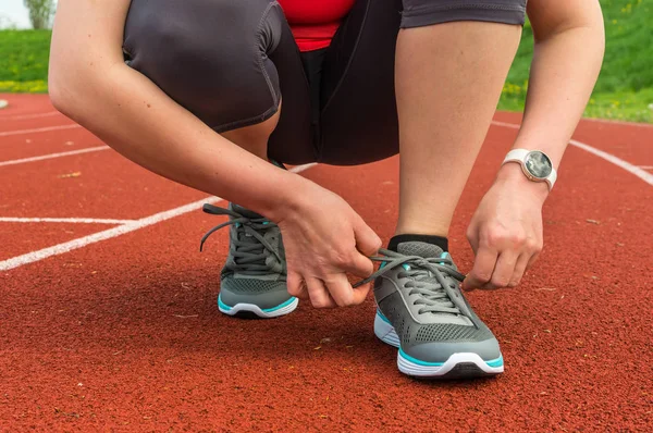 Woman is lacing her shoes on a stadium running track