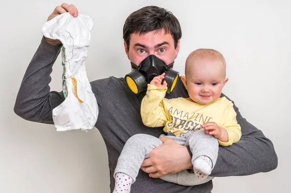 Father with gas mask is holding dirty diaper and little baby — Stock Photo, Image