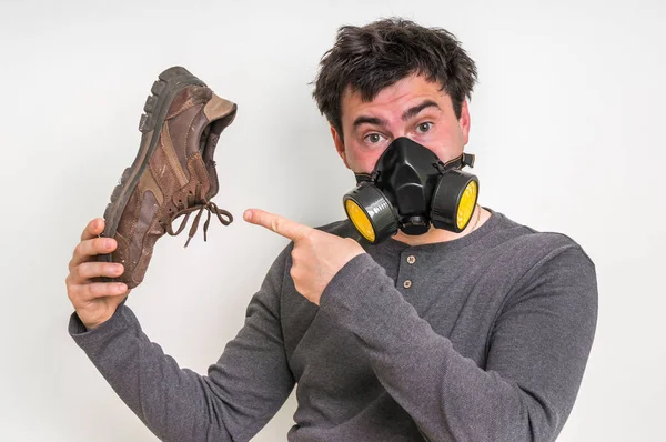 Man med gasmask håller smutsiga stinkande skor — Stockfoto