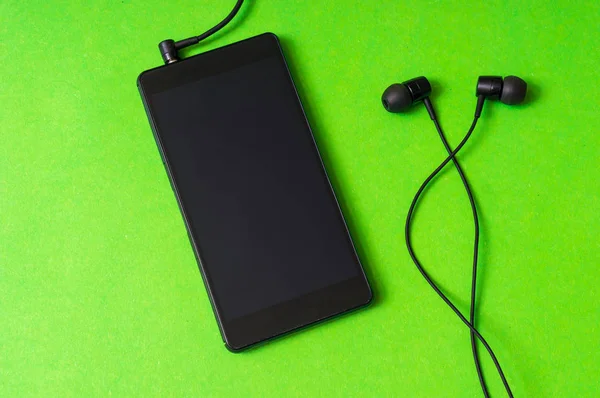 Мобильный телефон с наушниками на зеленом фоне — стоковое фото